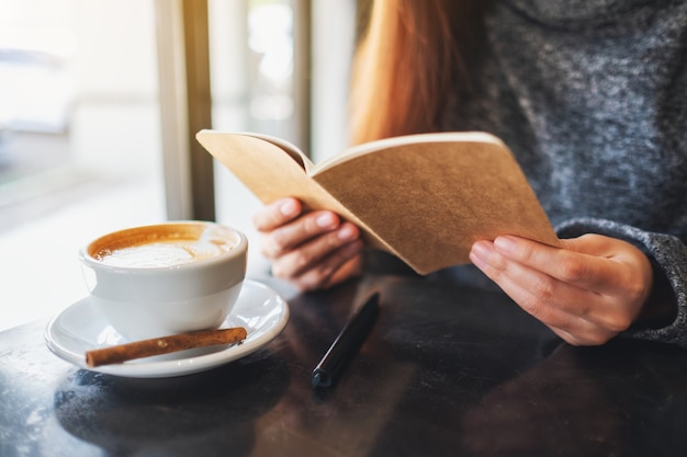 Image en gros plan d'une belle femme tenant et lisant un livre avec une tasse de café sur la table