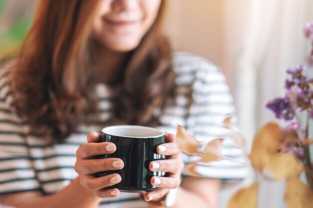 Image en gros plan d'une belle femme tenant une tasse noire de café chaud à boire