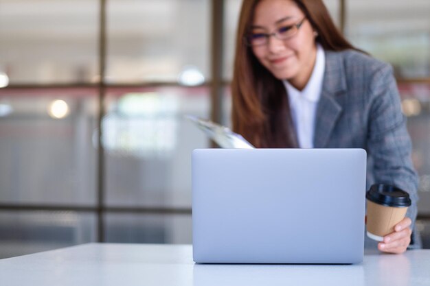 Image en gros plan d'une belle jeune femme d'affaires asiatique buvant du café et utilisant un ordinateur portable tout en travaillant au bureau