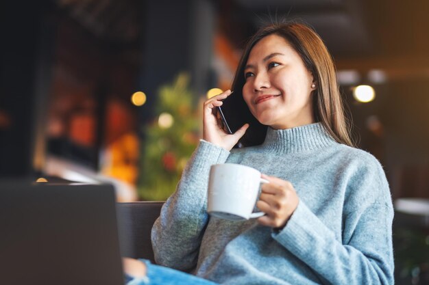 Image en gros plan d'une belle jeune femme asiatique parlant sur un téléphone portable tout en buvant du café