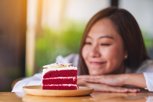 Image en gros plan d'une belle jeune femme asiatique regardant un morceau de gâteau de velours rouge dans un plateau en bois sur la table