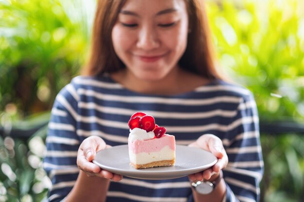 Image en gros plan d'une belle jeune femme asiatique tenant un morceau de gâteau au fromage aux fraises dans une assiette