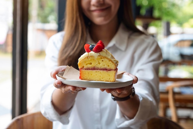 Image en gros plan d'une belle jeune femme asiatique tenant et servant un morceau de gâteau dans une assiette