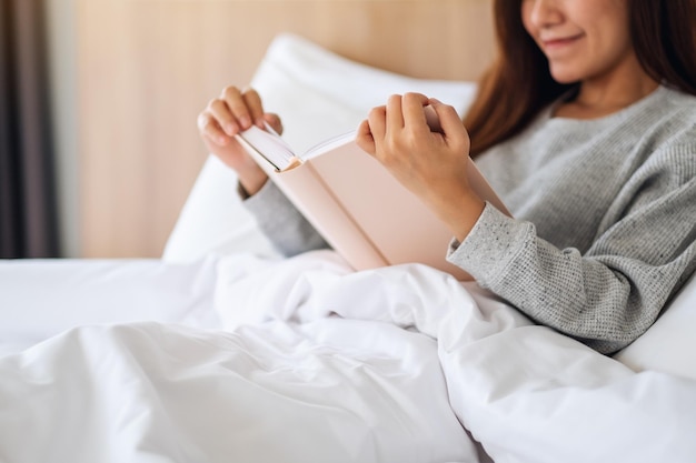 Image en gros plan d'une belle jeune femme lisant un livre dans un lit confortable blanc à la maison