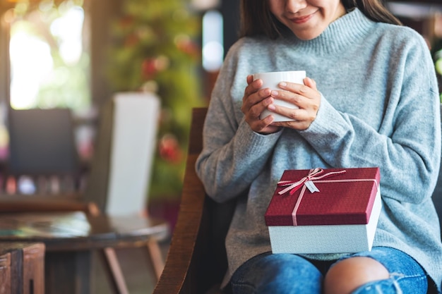 Image en gros plan d'une belle jeune femme tenant une boîte-cadeau tout en buvant du café