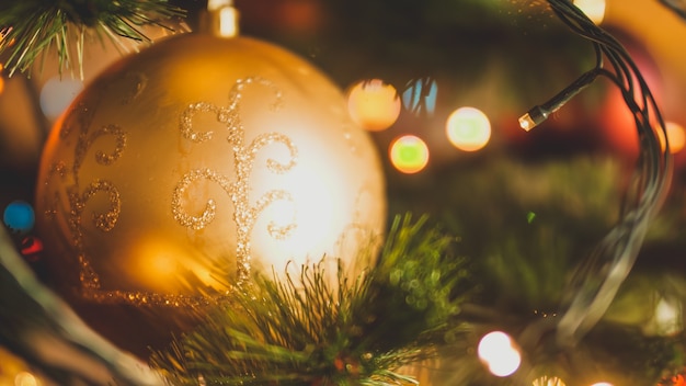 Image en gros plan de la boule de Noël dorée et des guirlandes lumineuses rougeoyantes sur l'arbre de Noël