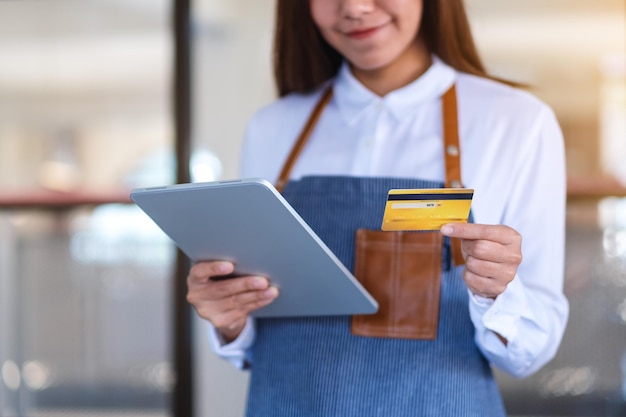 Image en gros plan d'une caissière tenant une carte de crédit tout en utilisant une tablette numérique