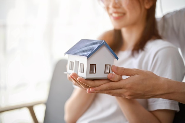 Image en gros plan d'un charmant jeune couple asiatique tenant ensemble un modèle de maison