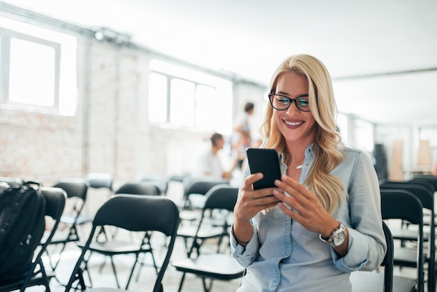 Image gros plan d&#39;une charmante femme blonde à l&#39;aide de téléphone portable dans la salle de conférence.