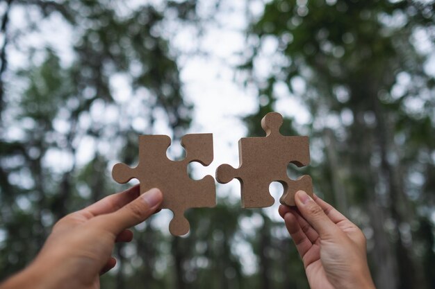 Image en gros plan d'un couple tenant et mettant un morceau de puzzle en bois ensemble à l'extérieur