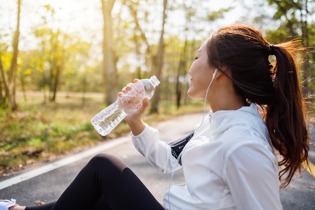 Image en gros plan d'une coureuse asiatique de l'eau potable de la bouteille après avoir fait du jogging dans le parc de la ville