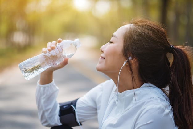 Image en gros plan d'une coureuse asiatique de l'eau potable de la bouteille après avoir fait du jogging dans le parc de la ville