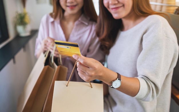 Image en gros plan de deux jeunes femmes tenant des sacs à provisions et une carte de crédit pour l'achat