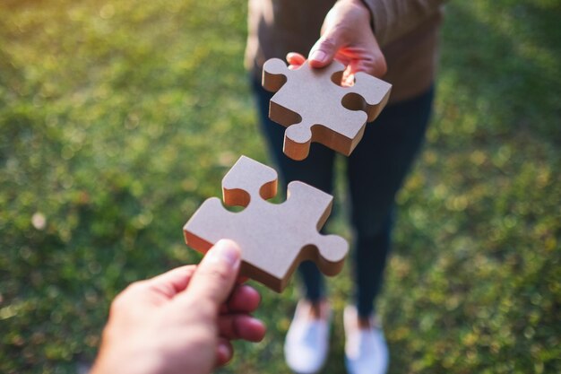 Image en gros plan de deux personnes tenant et assemblant un morceau de puzzle en bois