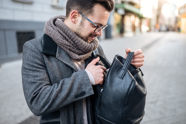 Image gros plan du jeune homme à la recherche dans le sac à dos à la rue de la ville.