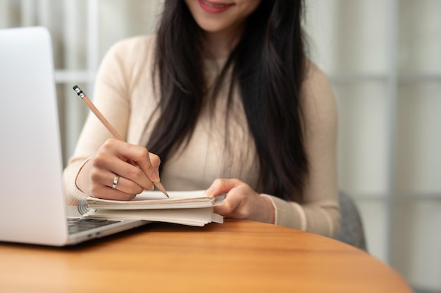 Image en gros plan d'une étudiante asiatique intelligente écrivant dans son cahier en faisant ses devoirs.