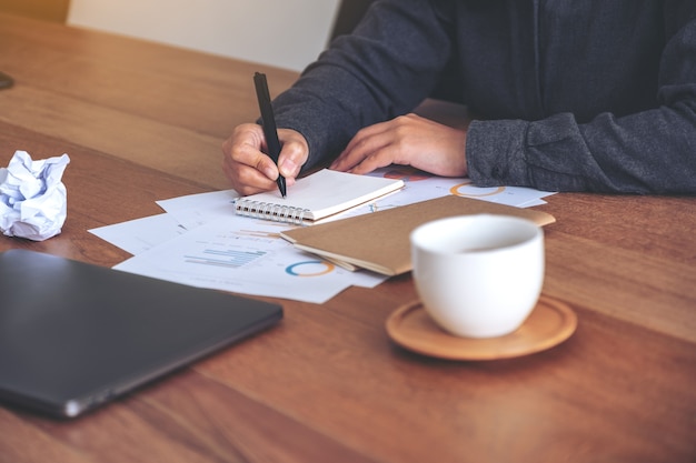 Image Gros plan d'une femme d'affaires travaillant et écrivant sur un cahier vierge blanc avec des papiers vissés et un ordinateur portable sur la table au bureau