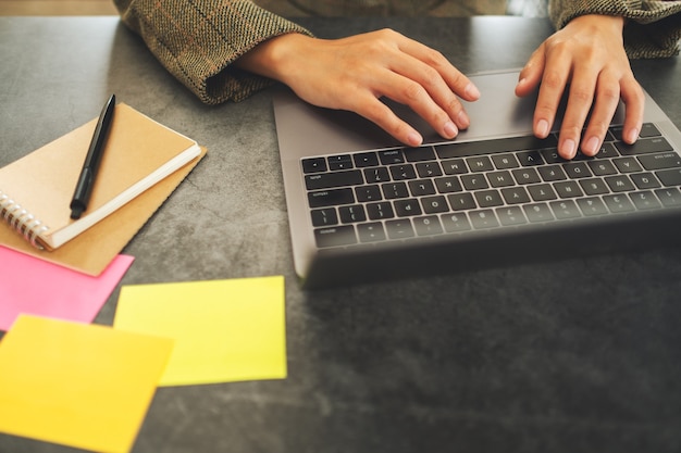 Image en gros plan d'une femme d'affaires utilisant et tapant sur un ordinateur portable avec des documents sur la table au bureau