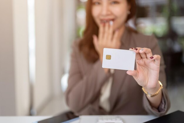 Photo image en gros plan d'une femme asiatique choquée et excitée montrant une carte de crédit ou de débit à la caméra alors qu'elle est assise à une table