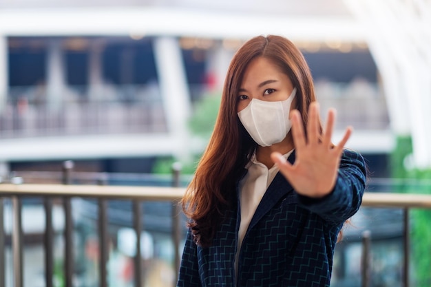 Image en gros plan d'une femme asiatique portant un masque protecteur, faisant un signe de la main d'arrêt pour empêcher la propagation de Covid-19 le concept de pandémie