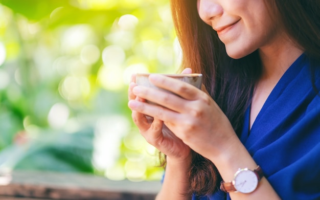 Image en gros plan d'une femme asiatique sentant et buvant du café chaud dans le jardin