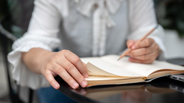 Une image en gros plan d'une femme assise à une table tenant un crayon et écrivant dans un cahier