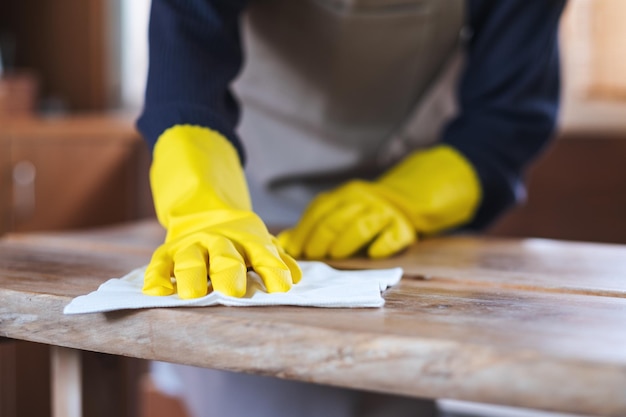 Image en gros plan d'une femme au foyer portant des gants de protection nettoyant et lavant une table en bois à la maison