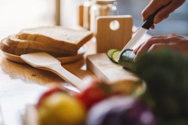 Image en gros plan d'une femme chef coupant et hachant des légumes au couteau sur une planche de bois dans la cuisine