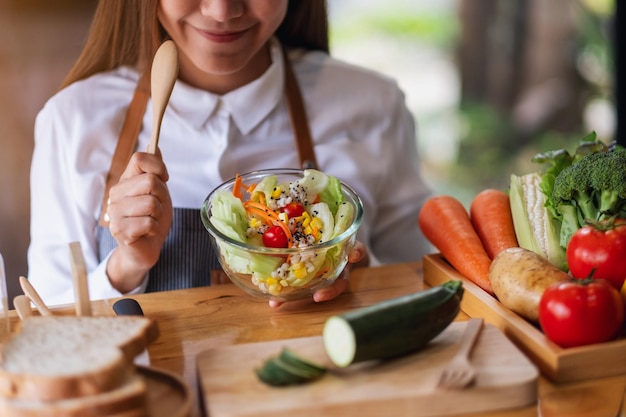 Image en gros plan d'une femme chef cuisinant une salade de légumes frais mélangés dans la cuisine