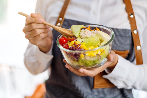 Image en gros plan d'une femme chef cuisinant et tenant un bol de salade de légumes frais à manger dans la cuisine