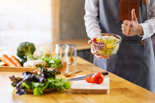 Image en gros plan d'une femme chef faisant et montrant le signe de la main pendant la cuisson d'une salade de légumes frais mélangés dans la cuisine