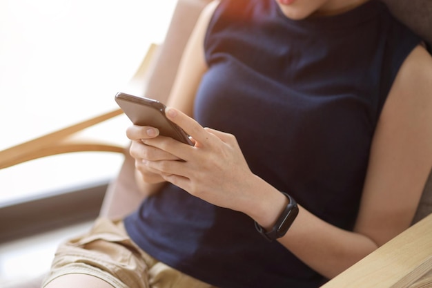 Image en gros plan Une femme détendue est assise dans un fauteuil confortable et utilise un smartphone dans le salon