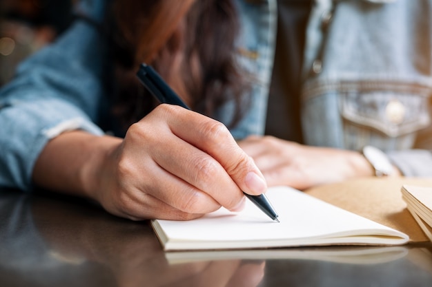 Image en gros plan d'une femme écrivant sur un cahier blanc sur une table en bois