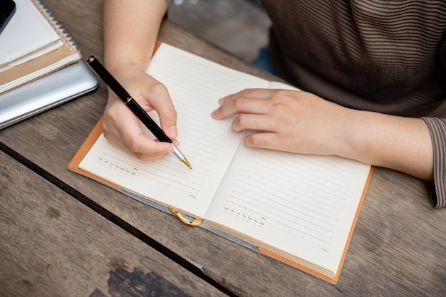 Une image en gros plan d'une femme écrivant quelque chose dans son cahier à un bureau en bois