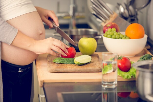 Image gros plan d'une femme enceinte coupant des légumes sur une planche de bois