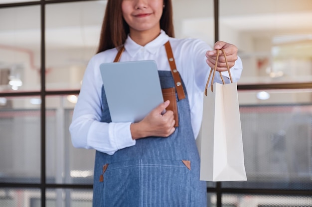 Image en gros plan d'une femme entrepreneur tenant une tablette numérique tout en donnant un sac à provisions au client