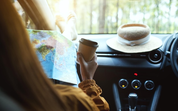 Image en gros plan d'une femme lisant une carte pour se diriger et boire du café dans la voiture