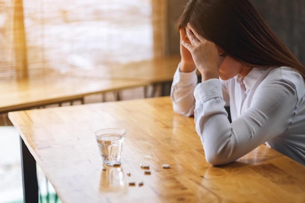 Image en gros plan d'une femme mal de tête avec des pilules blanches et un verre d'eau sur la table
