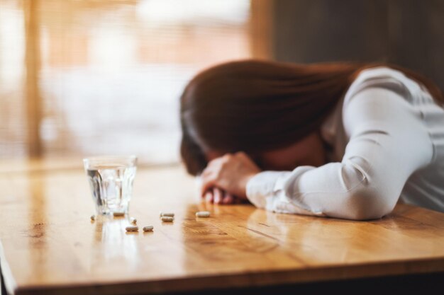 Image en gros plan d'une femme malade dormant sur une table avec des pilules blanches et un verre d'eau