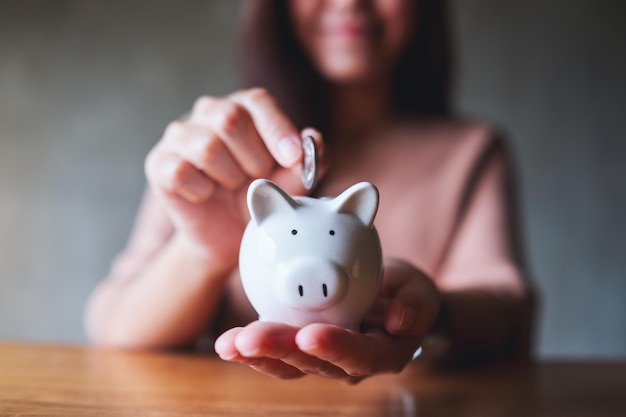 Image en gros plan d'une femme mettant des pièces dans une tirelire pour économiser de l'argent concept