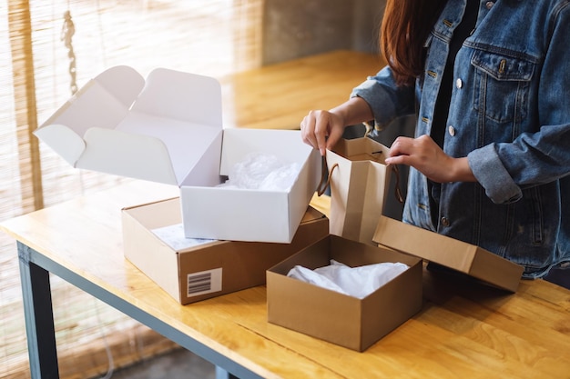 Image en gros plan d'une femme ouvrant et regardant à l'intérieur d'un sac à provisions avec une boîte à colis postal sur la table à la maison pour la livraison et le concept d'achat en ligne