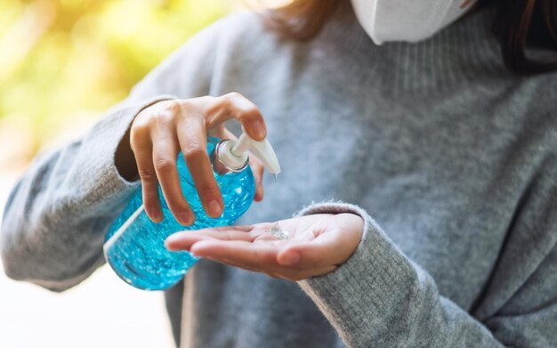 Image en gros plan d'une femme portant un masque de protection et appliquant un gel d'alcool pour se laver les mains pour les soins de santé et le concept de virus Covid-19 ou 2020