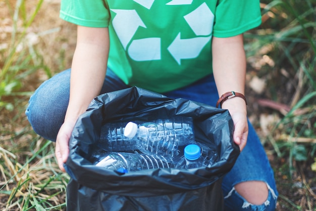 Photo image en gros plan d'une femme ramassant des bouteilles en plastique à ordures dans un sac en plastique pour le concept de recyclage