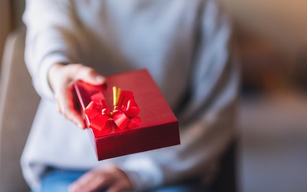 Image en gros plan d'une femme tenant et donnant une boîte cadeau rouge