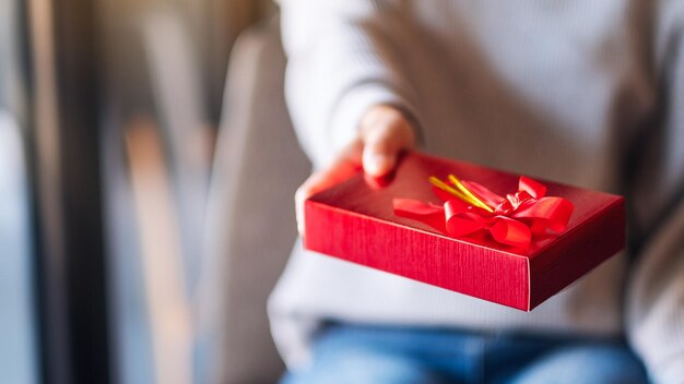 Image en gros plan d'une femme tenant et donnant une boîte cadeau rouge