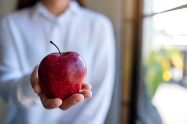 Image en gros plan d'une femme tenant et donnant une pomme rouge