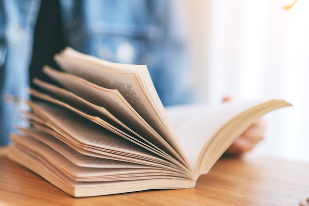 Image en gros plan d'une femme tenant et lisant un livre de roman vintage sur une table en bois