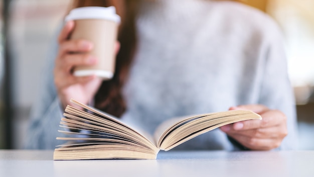 Image en gros plan d'une femme tenant et lisant un livre tout en buvant du café sur une table en bois