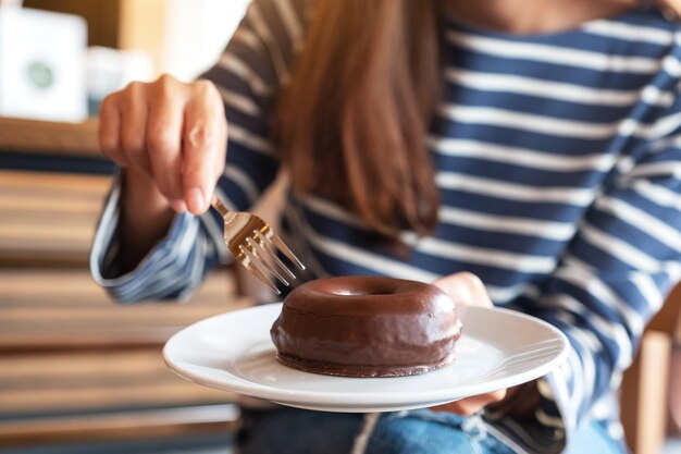 Image en gros plan d'une femme tenant et mangeant un beignet au chocolat