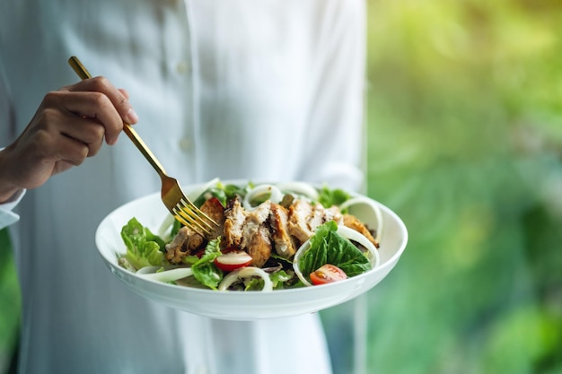 Image en gros plan d'une femme tenant et mangeant de la salade de poulet